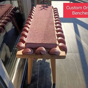 May include: A custom order bench with a pink velvet cushion and a wooden frame. The bench has a decorative trim of pink fabric rosettes around the edge of the cushion.  Custom Order Benches.