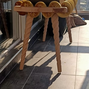 May include: A wooden bench with a rope-like design on the legs. The bench has a padded seat with a row of yellow velvet buttons. The bench is labeled "MADE BY CO. DESIGN".