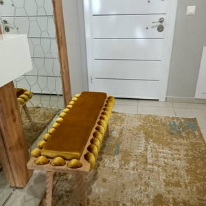 K&ouml;nnte beinhalten: Senfgelbe gepolsterte Bank mit rechteckiger Sitzfl&auml;che und einer Reihe dekorativer, abgerundeter Akzente. Die Bank hat hellfarbene Holzbeine mit gedrehtem Seildesign. Die Bank ist etwa 122 cm lang.