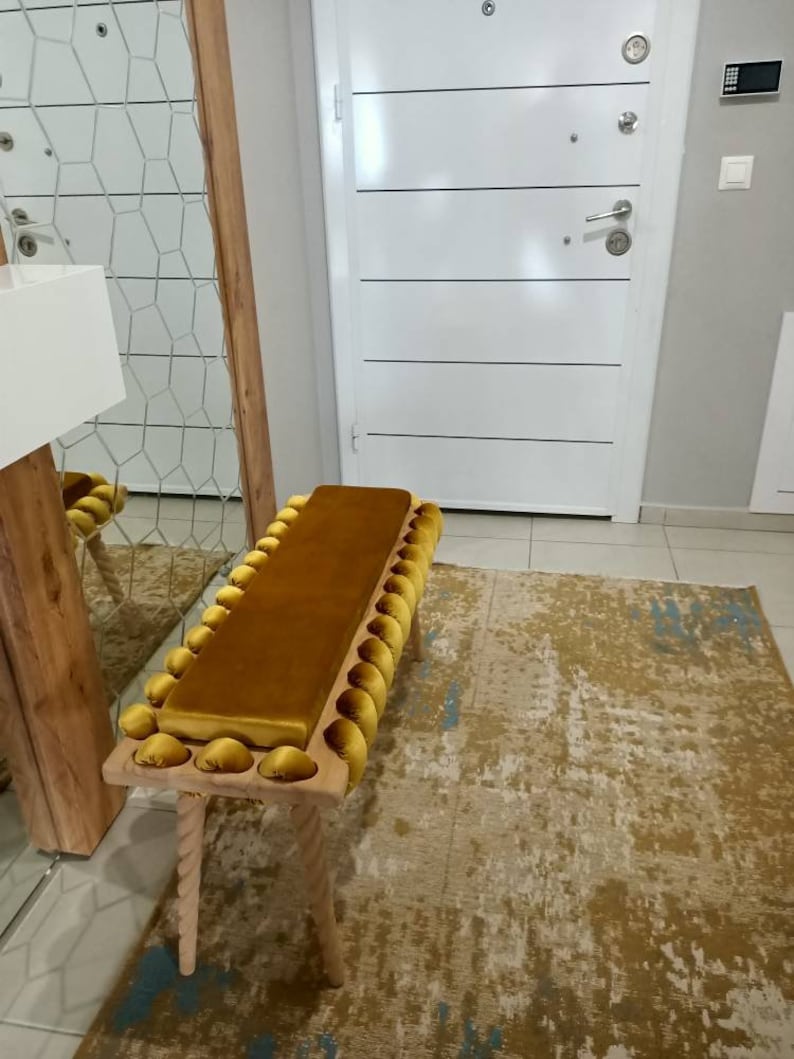 K&ouml;nnte beinhalten: Senfgelbe gepolsterte Bank mit rechteckiger Sitzfl&auml;che und einer Reihe dekorativer, abgerundeter Akzente. Die Bank hat hellfarbene Holzbeine mit gedrehtem Seildesign. Die Bank ist etwa 122 cm lang.