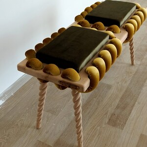 May include: A wooden bench with a unique design featuring a braided rope-like frame with gold velvet cushions. The bench has four twisted legs and a wooden top.
