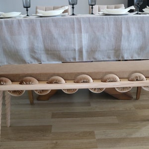 May include: A wooden bench with a brown velvet cushion and rope legs. The bench has a unique design with rounded edges and a series of small, rounded cushions along the front.