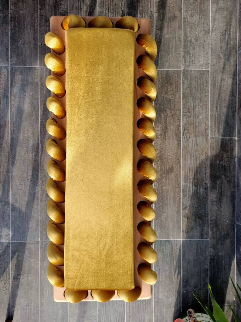 K&ouml;nnte beinhalten: Ein rechteckige, senfgelbe Samtbank mit Holzrahmen. Die R&auml;nder sind mit einer Reihe von goldenen, abgerundeten, dekorativen Elementen verziert. Die Bank steht vor einem Hintergrund aus grauem Fliesenboden. Ma&szlig;e: ca. 120 cm lang und 40 cm breit.