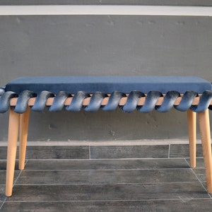 May include: A wooden bench with a dark blue velvet cushion. The cushion is braided around the edges of the bench.