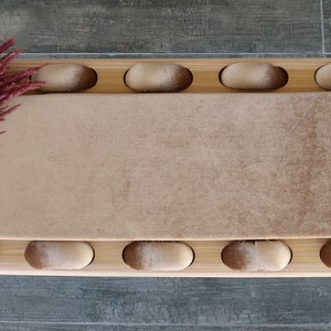 May include: A long, rectangular, wooden bench with a brown, plush cushion. The cushion has a gradient of color, starting with a light brown at one end and transitioning to a darker brown at the other end. The bench is decorated with a row of rounded, wooden knobs along the top and bottom edges.