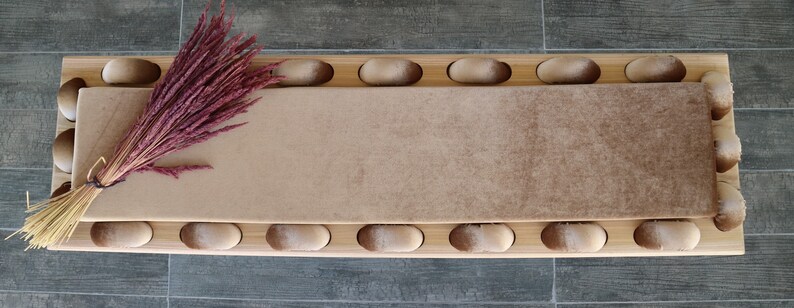 May include: A long, rectangular, wooden bench with a brown, plush cushion. The cushion has a gradient of color, starting with a light brown at one end and transitioning to a darker brown at the other end. The bench is decorated with a row of rounded, wooden knobs along the top and bottom edges.