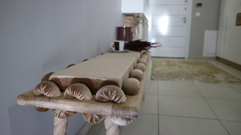 May include: A wooden console table with a beige velvet top and a decorative rope design on the legs. The table has a row of brown velvet buttons along the edge of the top.