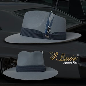 May include: A grey fedora hat with a black ribbon and a blue feather. The hat has a small label that says "Laric" on it. The hat is sitting on top of a black car.