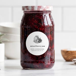 May include: A glass jar filled with dark red mixed berry jam, featuring a round white label with a black botanical illustration of berries and the text mixed berry jam, local & homegrown, made with love, by lily. The lid has a red checkered pattern.