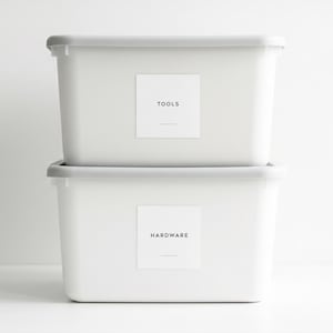 May include: Two stacked white plastic storage bins with lids. Each bin features a square white label with black text. The top label reads TOOLS and the bottom label reads HARDWARE. Text in the top left corner reads DESIGN: MINIMAL LABEL SIZE: 4" sq.