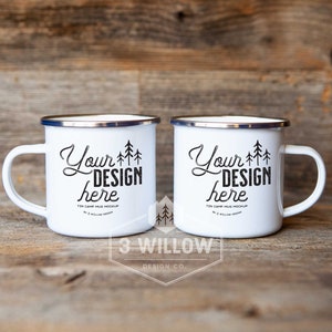 May include: Two white enamel mugs with black text and a silver rim. The text on the mugs reads "Your Design Here" and "Tin Camp Mug Mockup". The mugs are sitting on a wooden surface.