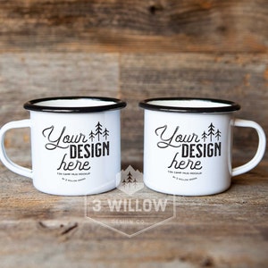 May include: Two white enamel camp mugs with black rims and handles. The mugs have the text "Your DESIGN here" in black script with a tree graphic. The mugs are on a wooden surface.