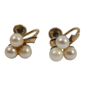 May include: A pair of gold tone clip-on earrings with three white pearls on each earring.