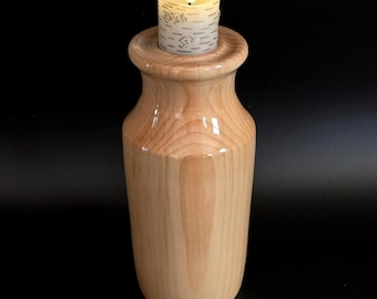 May include: A wooden candle holder with a light-colored finish. The holder has a wide, rounded top and a cylindrical body. A battery-operated candle with a flickering flame sits in the holder. The candle has a birch bark design.