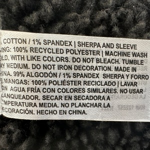 May include: A white fabric tag with black text detailing fabric composition and care instructions. The tag includes information about cotton, spandex, recycled polyester, and washing instructions. The tag also states "Made in China."