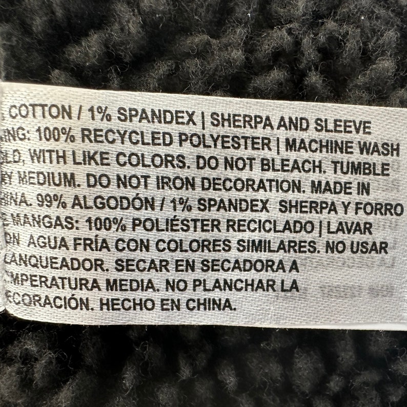 May include: A white fabric tag with black text detailing fabric composition and care instructions. The tag includes information about cotton, spandex, recycled polyester, and washing instructions. The tag also states "Made in China."