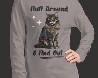 Puede incluir: Camiseta gris de manga larga con una ilustración de un gato marrón y negro y el texto "Fluff Around & Find Out".