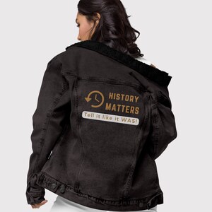 May include: A black denim jacket with a black faux fur collar. The back of the jacket features the text "HISTORY MATTERS" with a clock graphic and the phrase "Tell it like it WAS!"