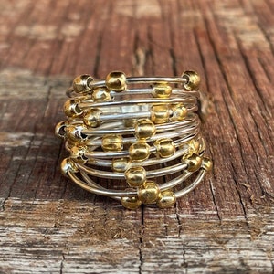 Puede incluir: Un anillo de oro y plata con múltiples bandas y cuentas doradas. El anillo está sobre una superficie de madera.