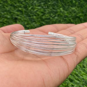 Puede incluir: Un brazalete de plata hecho de múltiples bandas finas apiladas.