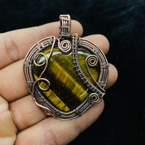 May include: A heart-shaped pendant wrapped in copper wire, featuring a tiger's eye gemstone at its centre.