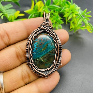 May include: A copper wire wrapped pendant featuring a green, blue, and brown oval shaped gemstone.