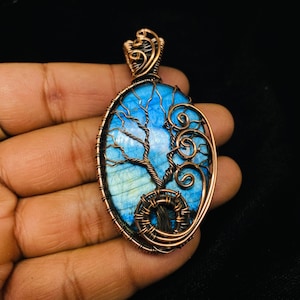 May include: A copper wire wrapped pendant featuring a blue labradorite stone with a tree design. The pendant is oval shaped and has a copper bail for hanging.