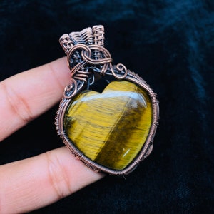 May include: A copper wire wrapped heart-shaped pendant with a tiger's eye gemstone.