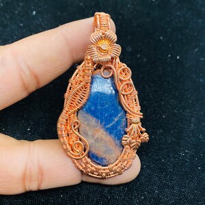 May include: A copper wire wrapped pendant featuring a blue and white gemstone with a copper flower accent.