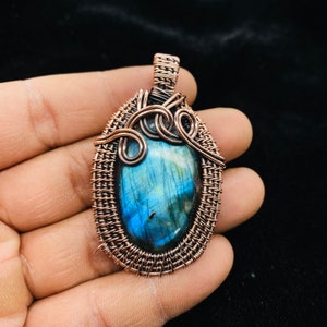 Peut inclure: Un pendentif en fil de cuivre enveloppé avec une pierre précieuse de labradorite bleue et verte. Le pendentif a un design en fil tissé avec un détail en spirale.
