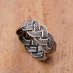 Peut inclure: Une bague argentée et cuivrée avec un motif de nœud celtique. La bague présente un motif entrelacé de métal argenté et cuivré, créant un aspect texturé et détaillé. La bague est un bijou.
