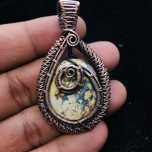 May include: A copper wire wrapped pendant featuring a brown, white and yellow patterned stone.