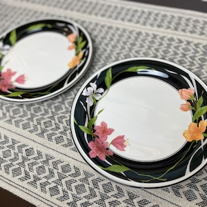 Op de afbeelding: Twee zwarte en witte bloembedinerborden met een wit centrum en een zwarte rand. De borden hebben een bloemenontwerp met roze, oranje en witte bloemen.