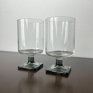 May include: Two clear glass drinking glasses with square bases. The bases are a dark gray color.