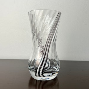 Puede incluir: Un jarrón de vidrio transparente con un patrón de espiral en blanco y negro. El jarrón tiene una base ancha y un cuello estrecho.