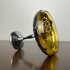 Puede incluir: Un plato con pie de vidrio ámbar y plateado con un diseño decorativo de corte. El plato está sobre una superficie de madera.