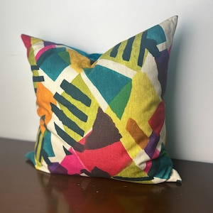 May include: A colorful geometric patterned throw pillow with a white background. The pattern features teal, green, yellow, orange, pink, purple, and brown.