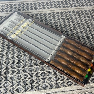 Puede incluir: Una caja de seis tenedores para fondue con mangos de madera. La caja está etiquetada como "Fondue Forks" con el texto "Deluxe Stainless Steel with Keyaki Wood Handles".