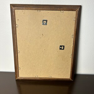 K&ouml;nnte beinhalten: Die R&uuml;ckseite eines braunen Holzbildrahmens mit zwei Metall-Aufh&auml;ngungshaken.