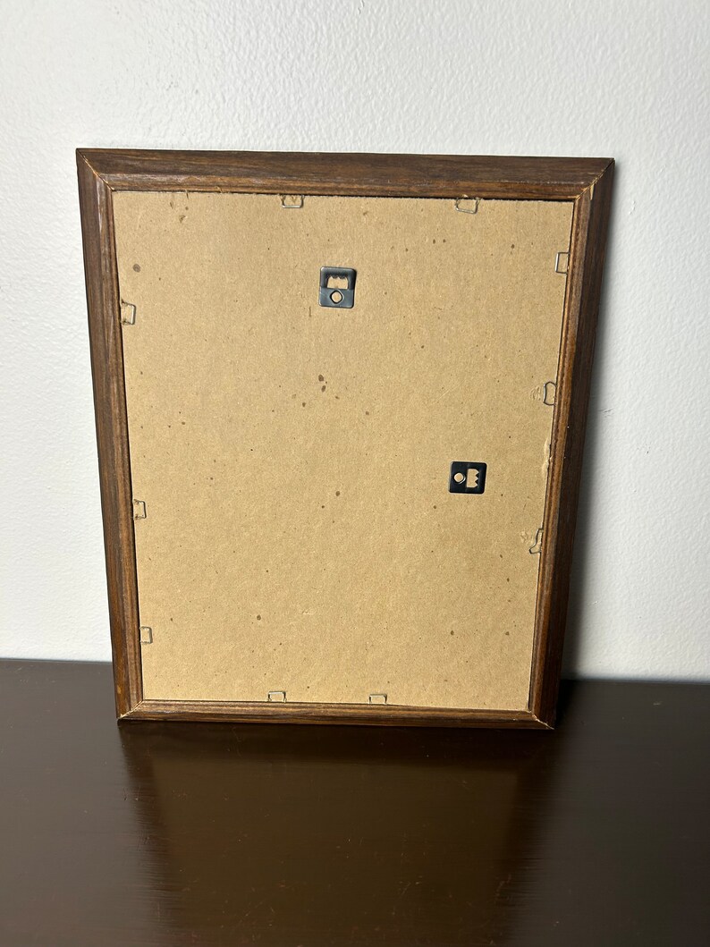 K&ouml;nnte beinhalten: Die R&uuml;ckseite eines braunen Holzbildrahmens mit zwei Metall-Aufh&auml;ngungshaken.