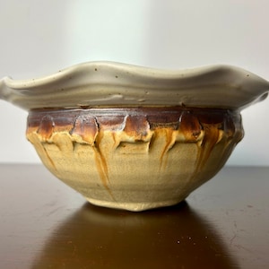 May include: A handmade ceramic bowl with a white glaze and brown accents. The bowl has a wavy rim and a textured exterior.