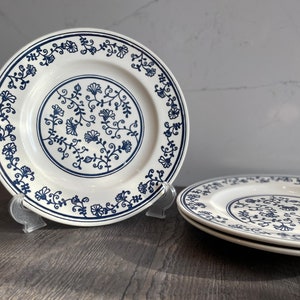 Puede incluir: Dos platos de cerámica blanca con un patrón floral azul. Los platos están apilados uno encima del otro.
