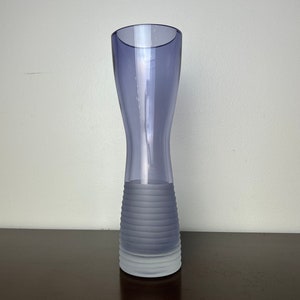 May include: A clear glass vase with a frosted, textured base. The vase is a light purple color and has a narrow neck and a wide base.