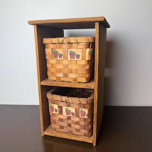 May include: A wooden storage unit with two woven baskets. The baskets are rectangular and feature apple-themed accents. The unit is made of light brown wood and has a simple, rectangular design, suitable for various storage needs.