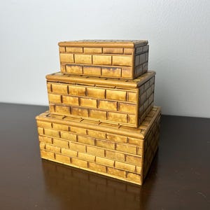 May include: Three stacked wooden boxes with a brick pattern. The boxes are all the same size and shape, and they are made of a light brown wood.