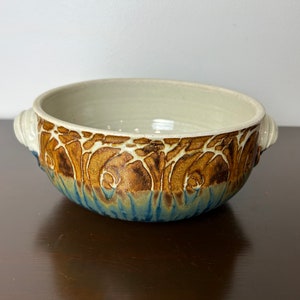 May include: A white ceramic bowl with brown and blue glaze. The bowl has two handles and a decorative design around the rim.
