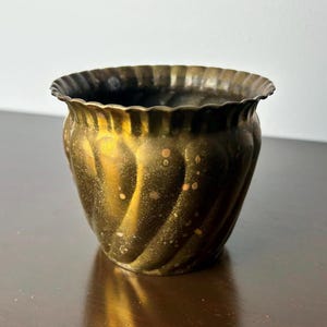 Könnte beinhalten: Ein kleiner, goldfarbener Metalltopf mit geriffeltem Design. Der Topf hat eine leicht abgenutzte Oberfläche.