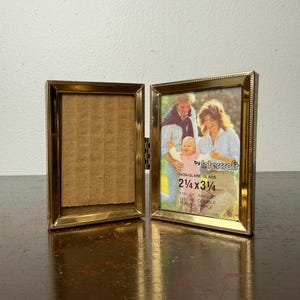 May include: A vintage gold-toned metal double picture frame, one side open, the other displaying a family photo. The frame is labeled "by Intercraft" and the photo is 2 1/4 x 3 3/4 inches.