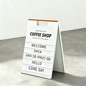 May include: A white A-frame sign for a coffee shop with the text "COFFEE SHOP" and "THE BEST SPOT FOR A BREW". Additional text includes "WELCOME", "OPEN", "AM9:30-PM21:00", "HELLO", and "COME SAY". The top is wooden.