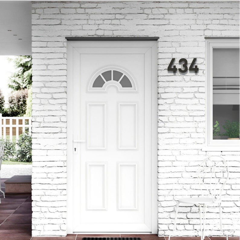 May include: A white front door with a half-circle window at the top and rectangular panels. The number "434" is displayed in black on the white brick wall. A white chair sits nearby.
